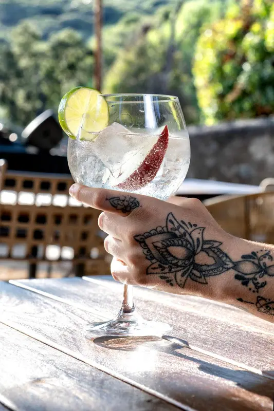 Un cocktail rafraîchissant dans un verre, tenu par une main tatouée.