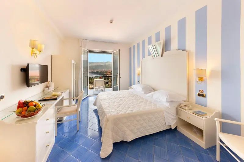 Chambre lumineuse avec un lit blanc et une vue sur la mer.