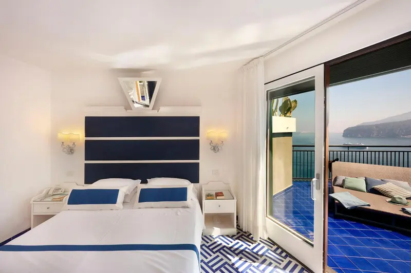 Chambre lumineuse avec un lit double et une vue sur la mer depuis une terrasse.