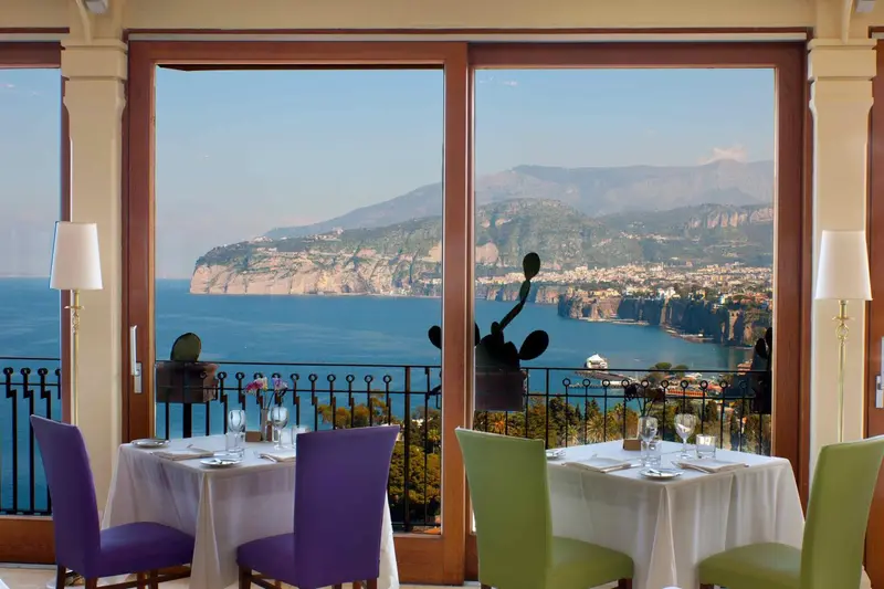 Tables dressées devant une grande baie vitrée donnant sur la mer et les montagnes.
