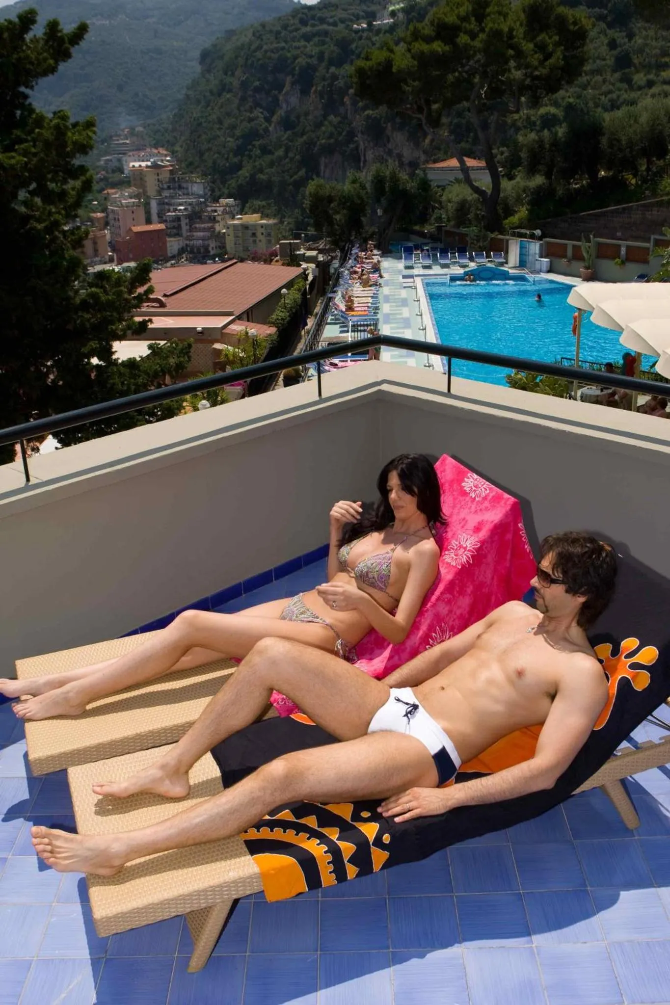 Un couple se relaxe sur des transats au bord d'une piscine ensoleillée.
