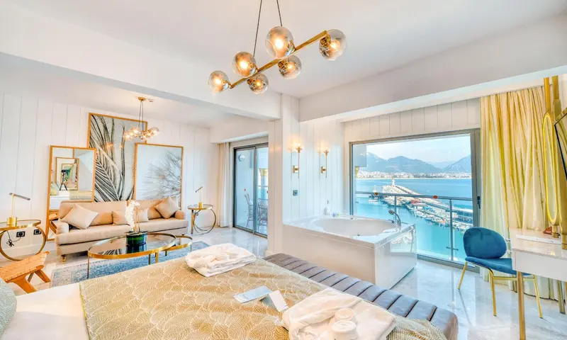 Une chambre spacieuse avec un lit king-size, un canapé et une baignoire à remous donnant sur la mer.
