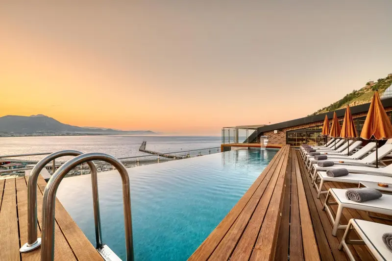 Une piscine à débordement offre une vue sur la mer et les montagnes au coucher du soleil.