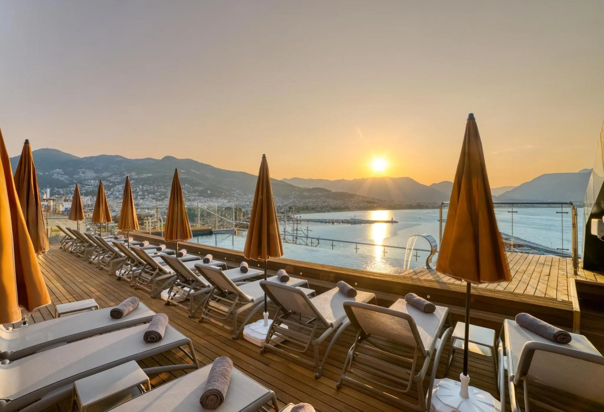 Terrasse avec transats et parasols dominant une vue sur la mer au coucher du soleil.