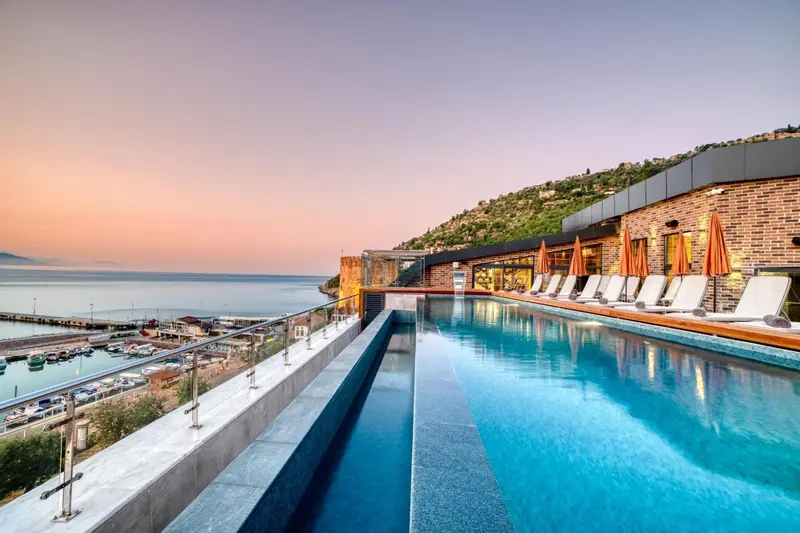 Une piscine à débordement surplombe la mer et un port de plaisance au coucher du soleil.