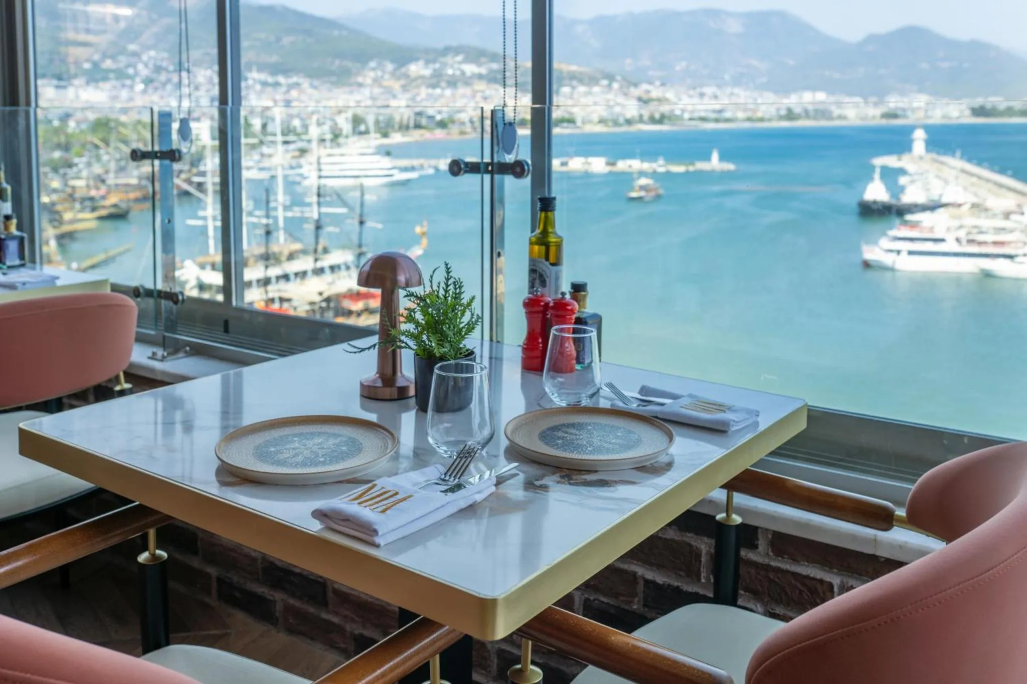 Table dressée dans un restaurant avec vue sur un port de plaisance et la mer.