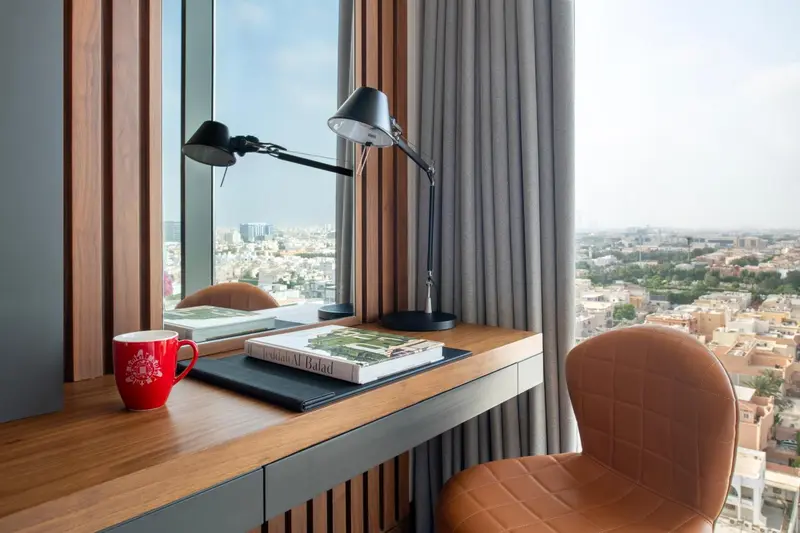 Un bureau en bois avec une lampe et une tasse près d'une fenêtre donnant sur une ville.