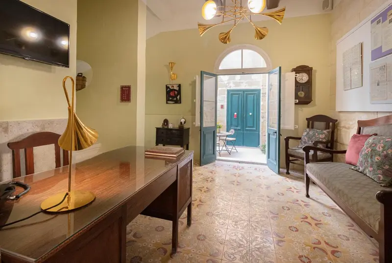 Une pièce lumineuse avec un bureau en bois et un canapé près d'une porte ouverte sur une cour.