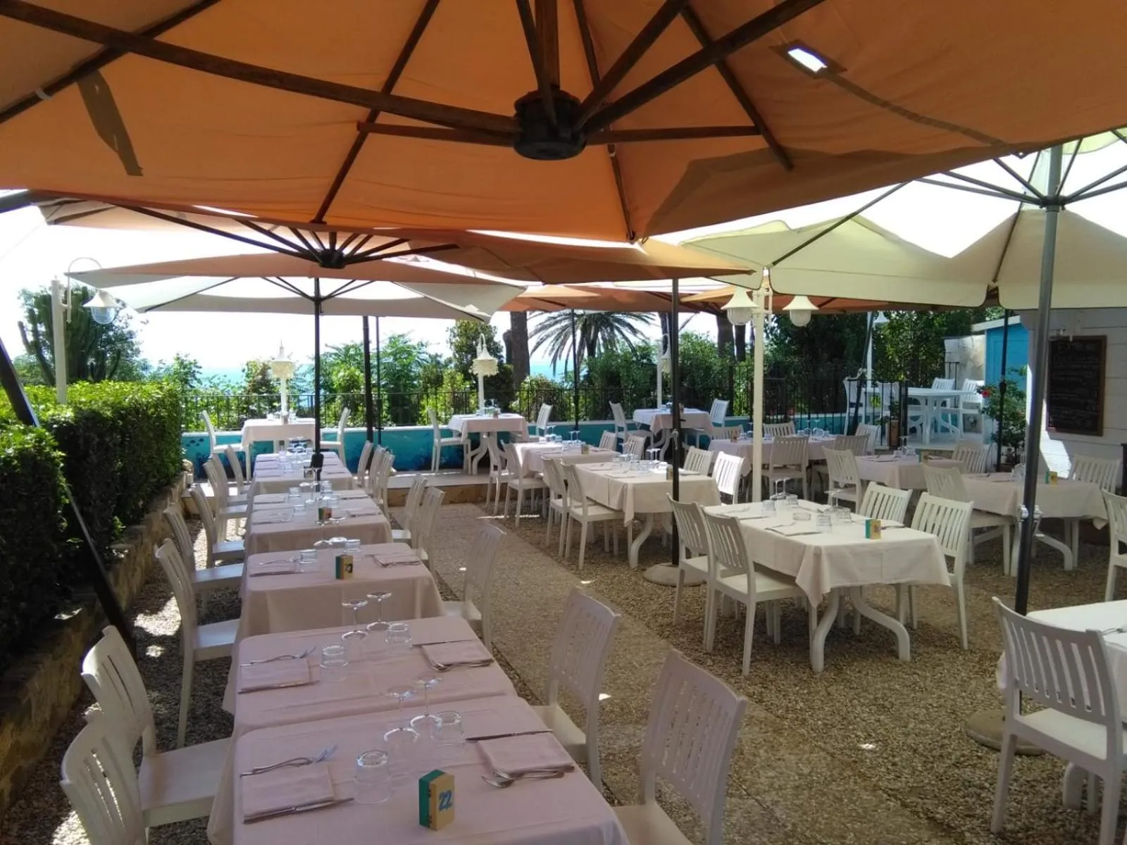 Terrasse ombragée avec tables et chaises blanches dressées pour un repas.