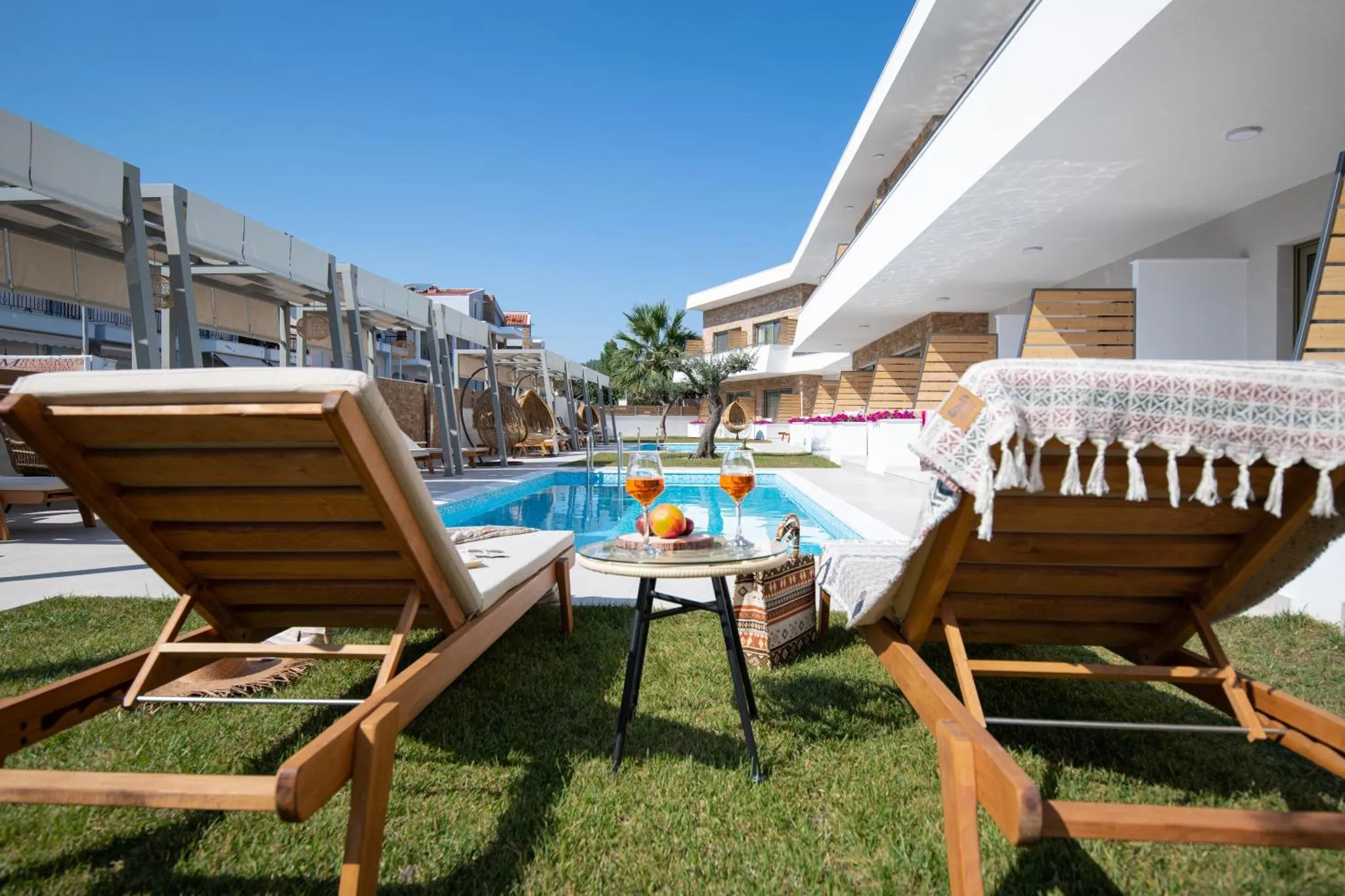 Deux transats avec des verres sur une table basse près d'une piscine ensoleillée.