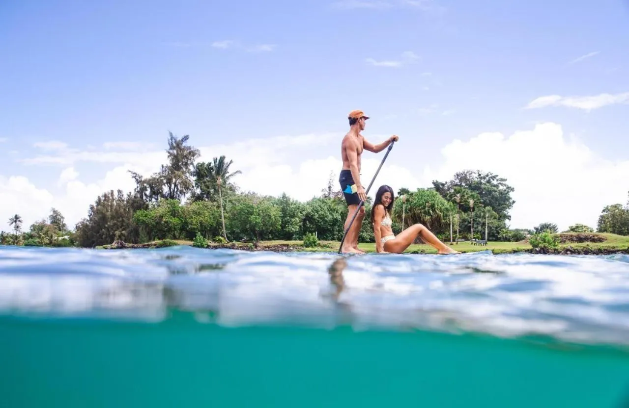 Un couple pratique le stand-up paddle sur une eau turquoise.