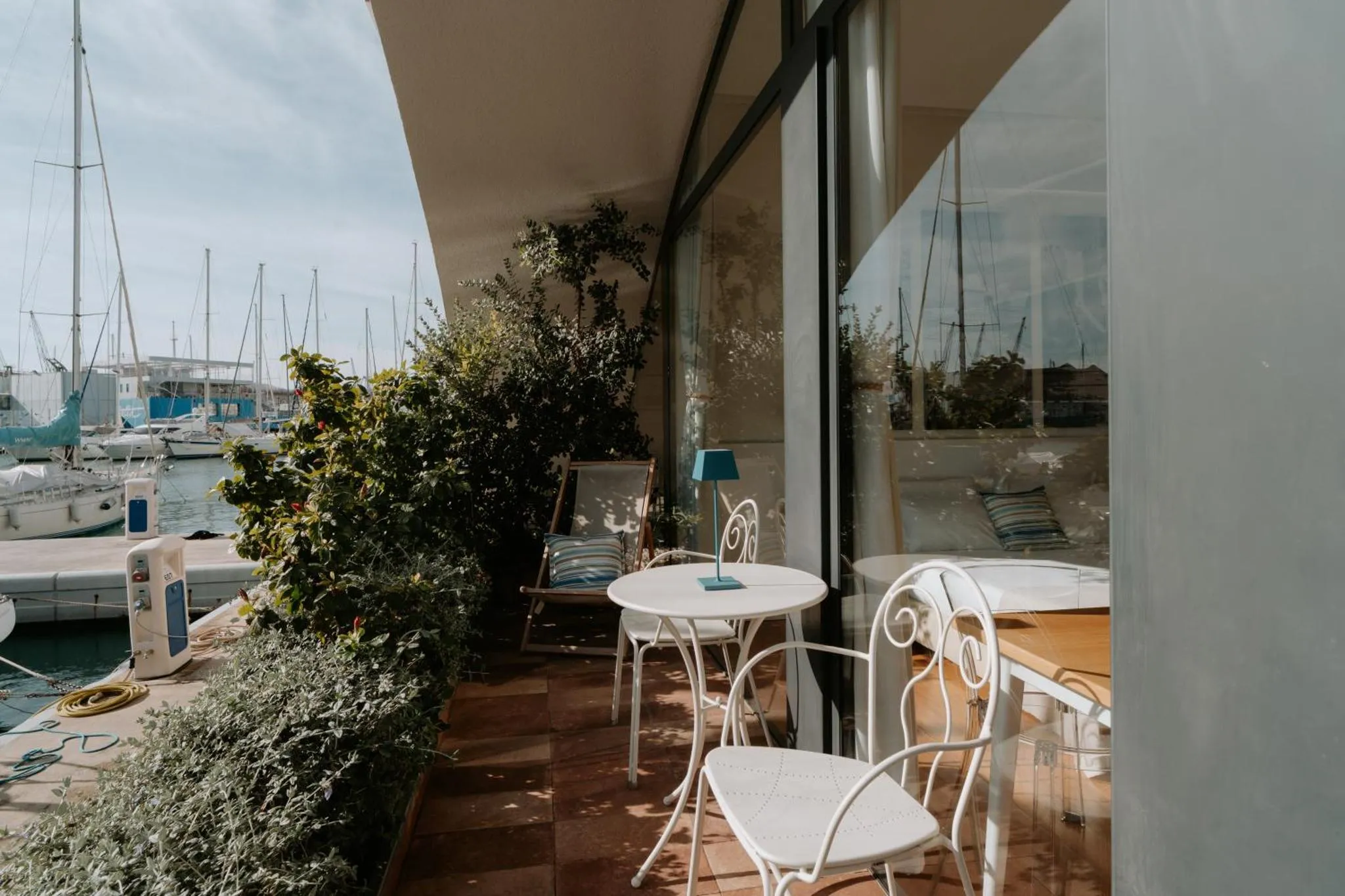 Terrasse ombragée avec tables et chaises donnant sur un port de plaisance.