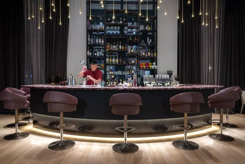 Un barman prépare un cocktail derrière un comptoir illuminé.