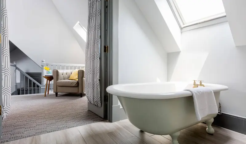 Une baignoire sur pieds se trouve dans une pièce mansardée avec un coin salon.