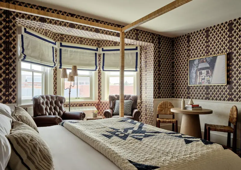 Une chambre à coucher avec un lit recouvert d'une courtepointe et deux fauteuils en cuir près d'une fenêtre.