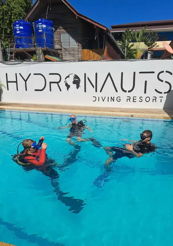 Des personnes en équipement de plongée s'entrainent dans une piscine turquoise.
