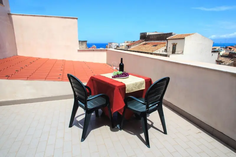 Une table avec une bouteille de vin et des fruits est dressée sur une terrasse ensoleillée.