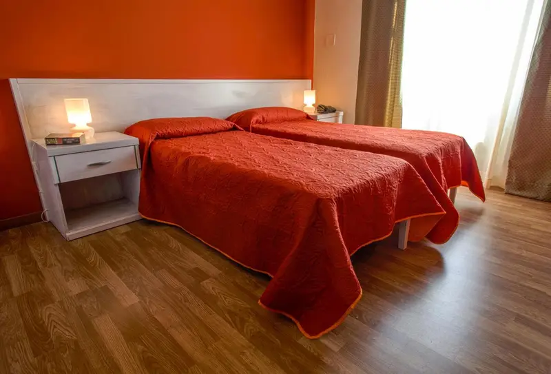 Une chambre avec deux lits simples recouverts d'une courtepointe rouge.