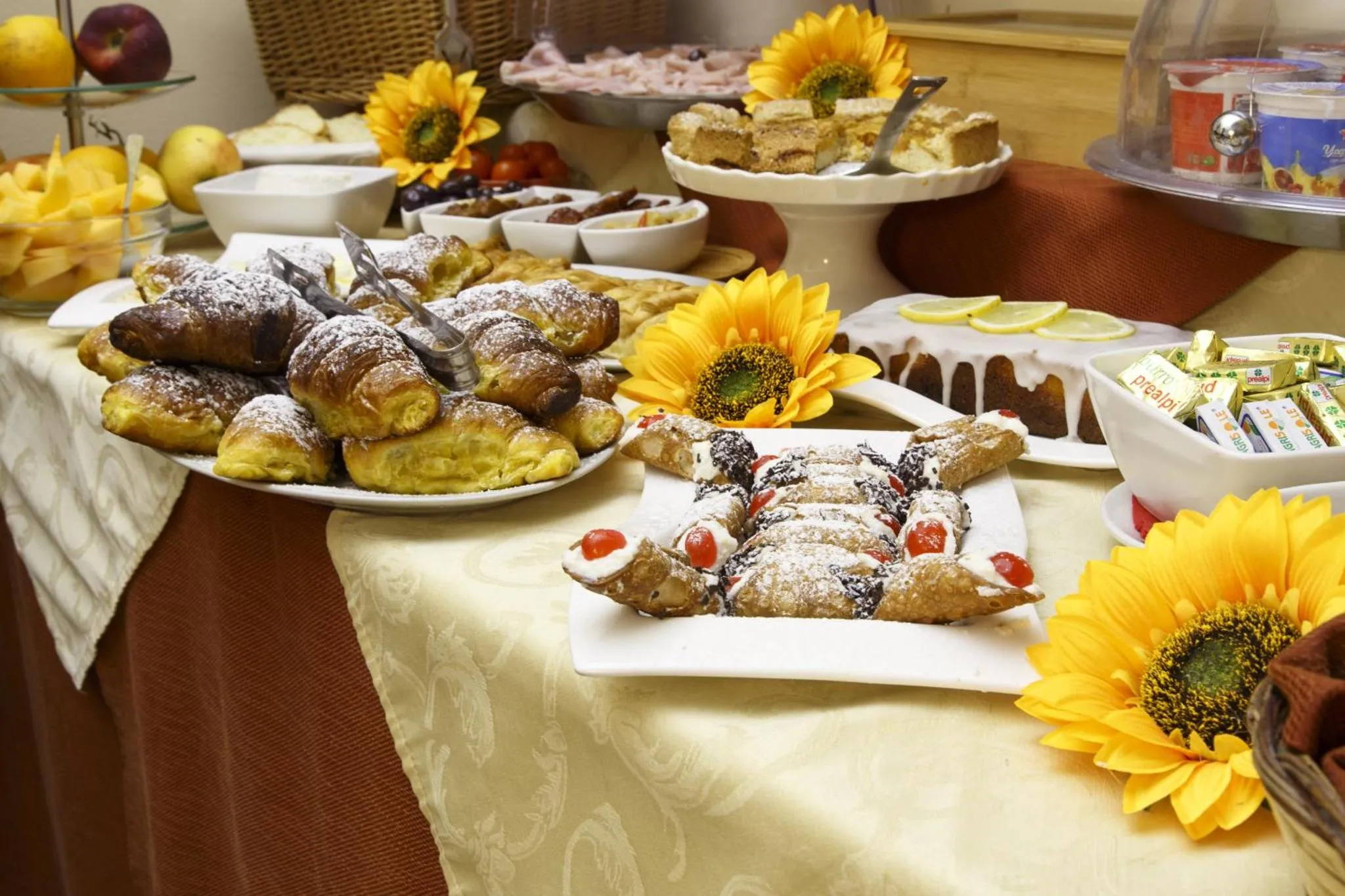 Une table garnie de pâtisseries et de fruits frais est décorée de tournesols.