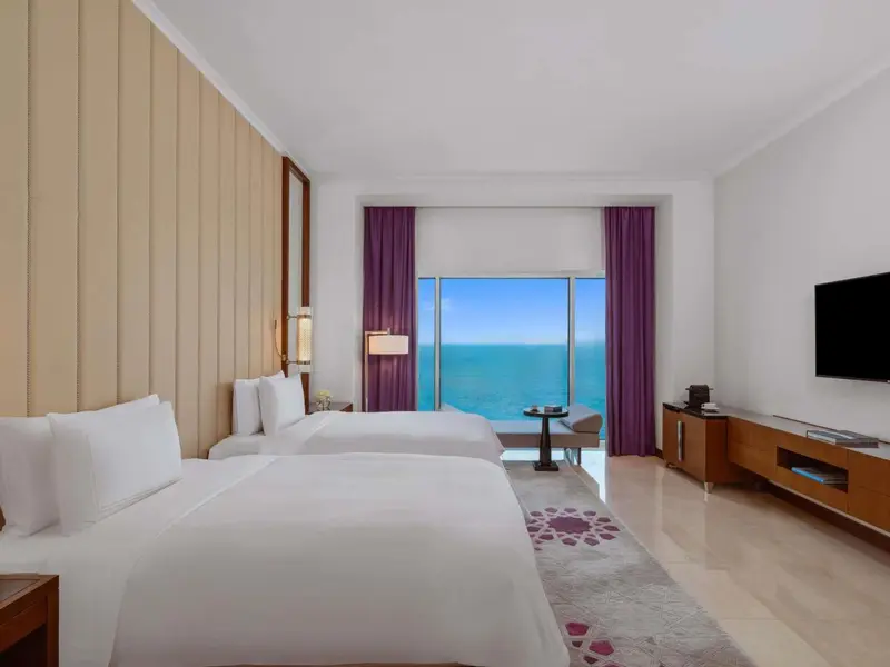 Chambre lumineuse avec deux lits et vue sur la mer.