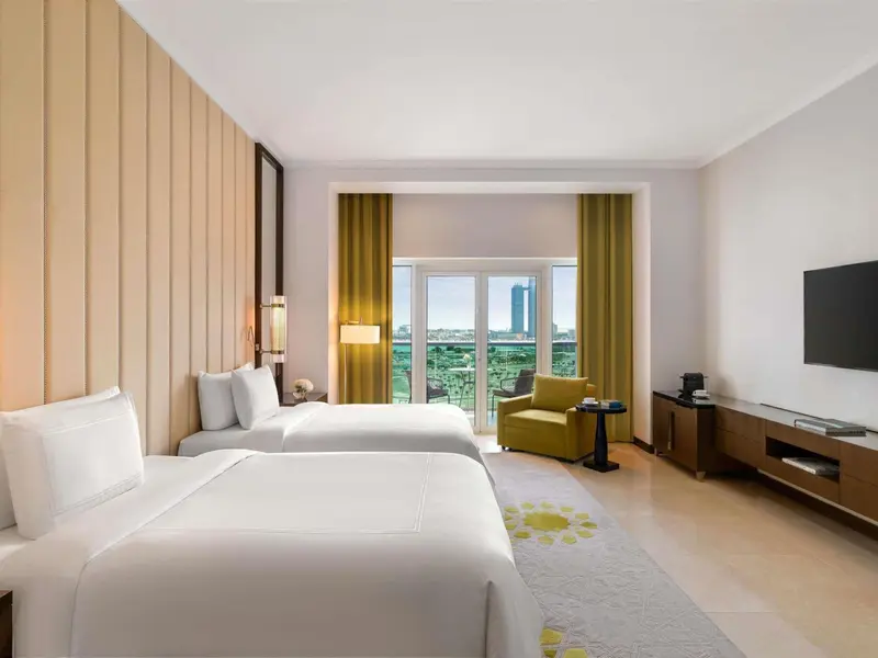 Chambre lumineuse avec deux lits simples et un coin salon près d'une fenêtre.