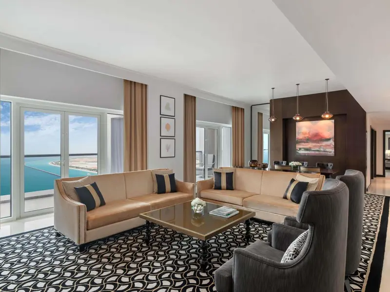 Un grand salon lumineux avec un canapé d'angle et des fauteuils face à de larges baies vitrées.