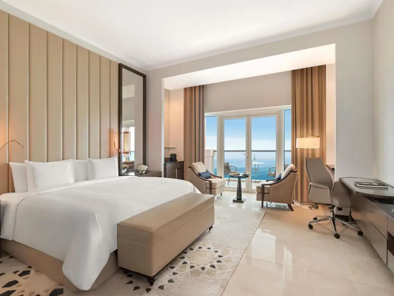 Chambre lumineuse avec un grand lit et un espace salon donnant sur la mer.