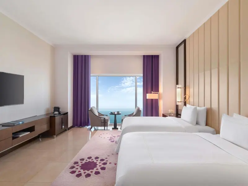 Chambre lumineuse avec deux lits et vue sur la mer.