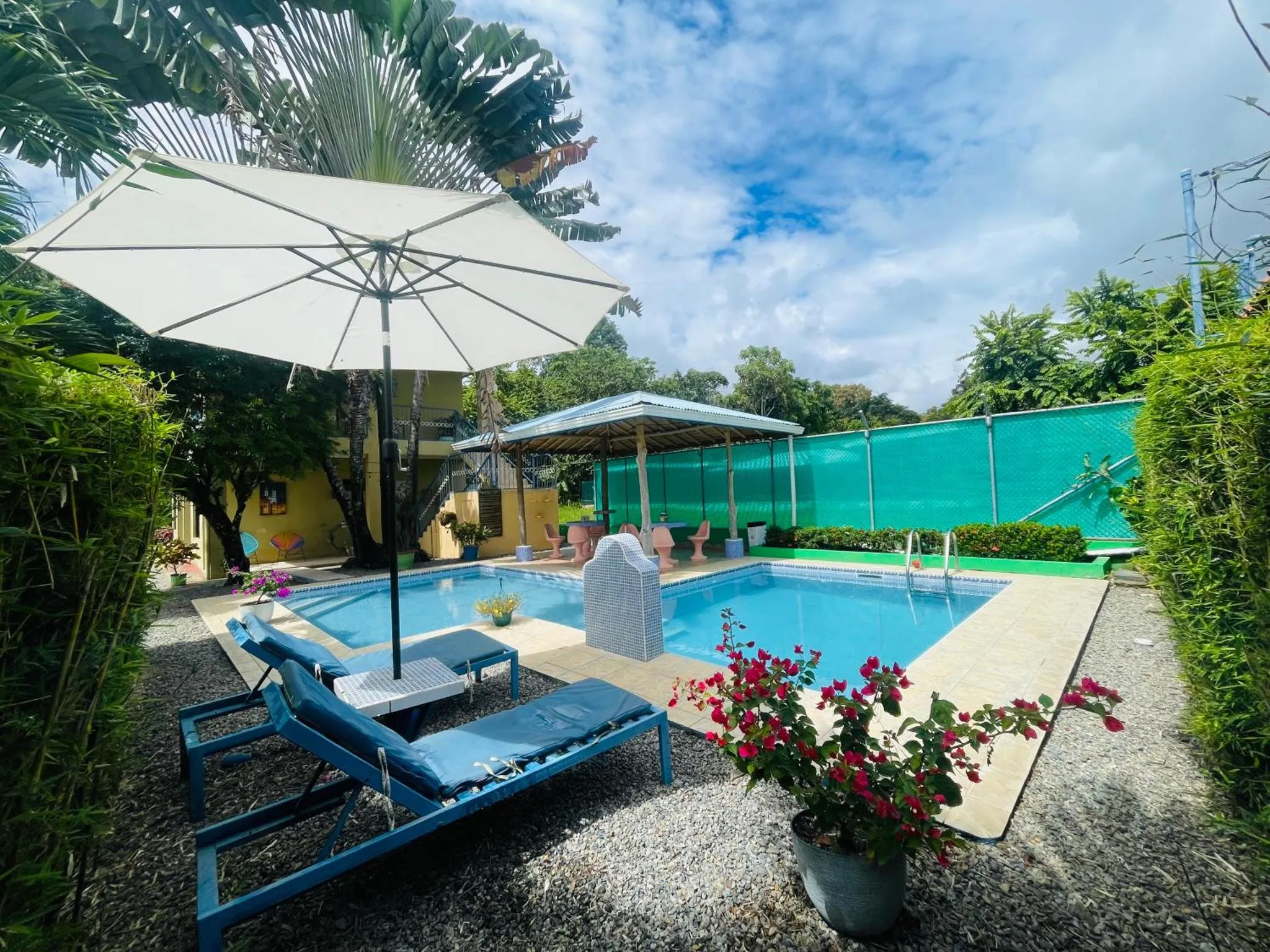 Transats bleus disposés au bord d'une piscine turquoise ombragée par un parasol.