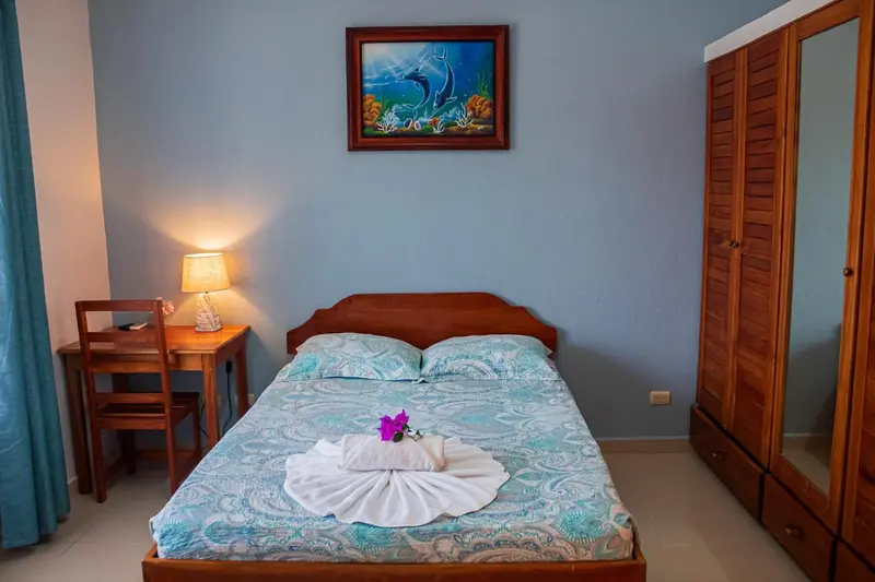 Une chambre lumineuse avec un lit recouvert d'une courtepointe turquoise et d'une décoration florale.