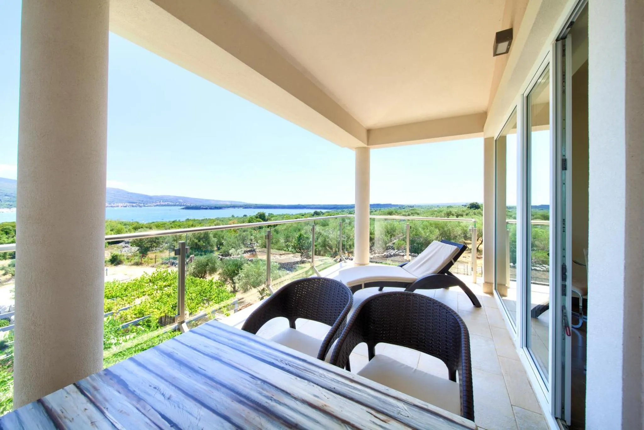 Une terrasse avec table et chaises offre une vue sur la mer et la végétation.