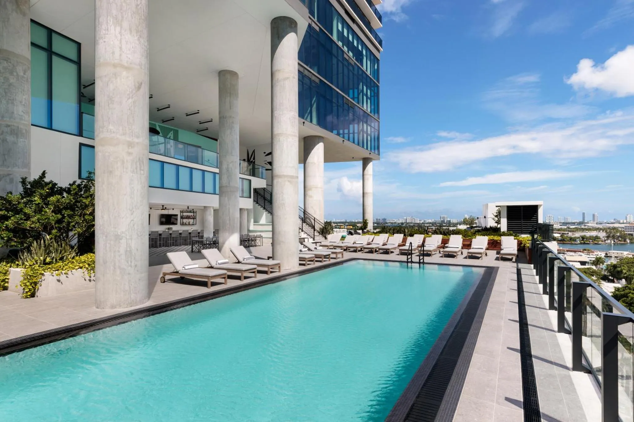Une piscine rectangulaire avec des transats et des palmiers, devant un bâtiment moderne.