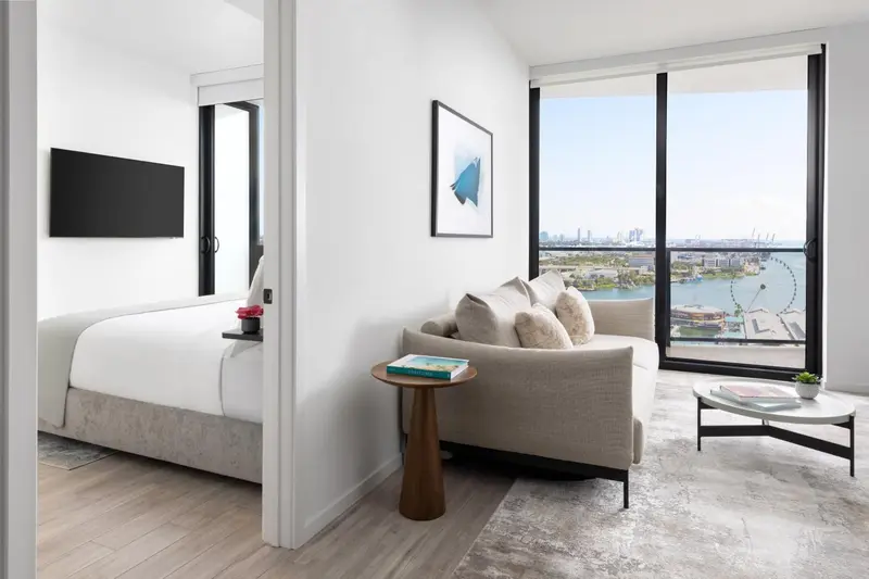 Espace de vie lumineux avec canapé et lit près d'une grande fenêtre.