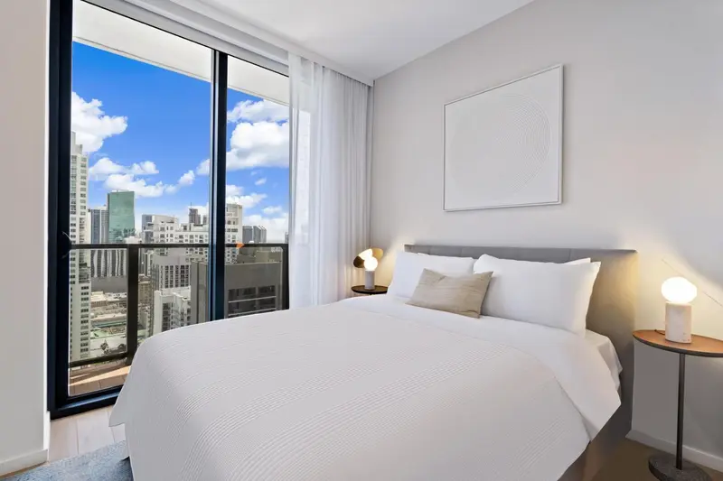 Chambre lumineuse avec un grand lit et une vue sur la ville.