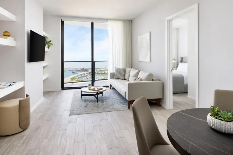 Un salon lumineux s'ouvre sur une chambre à travers une porte ouverte.