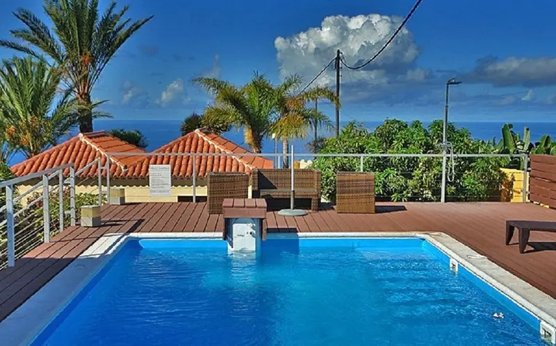Petite piscine turquoise entourée d'une terrasse en bois et de végétation luxuriante.