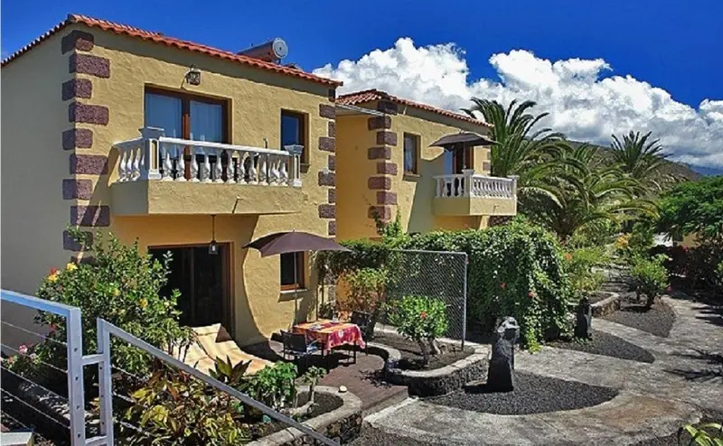 Façade jaune d'une maison avec balcon et jardin fleuri.