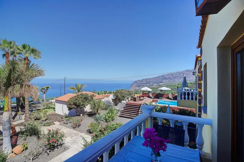 Vue d'une terrasse fleurie sur un paysage côtier ensoleillé.
