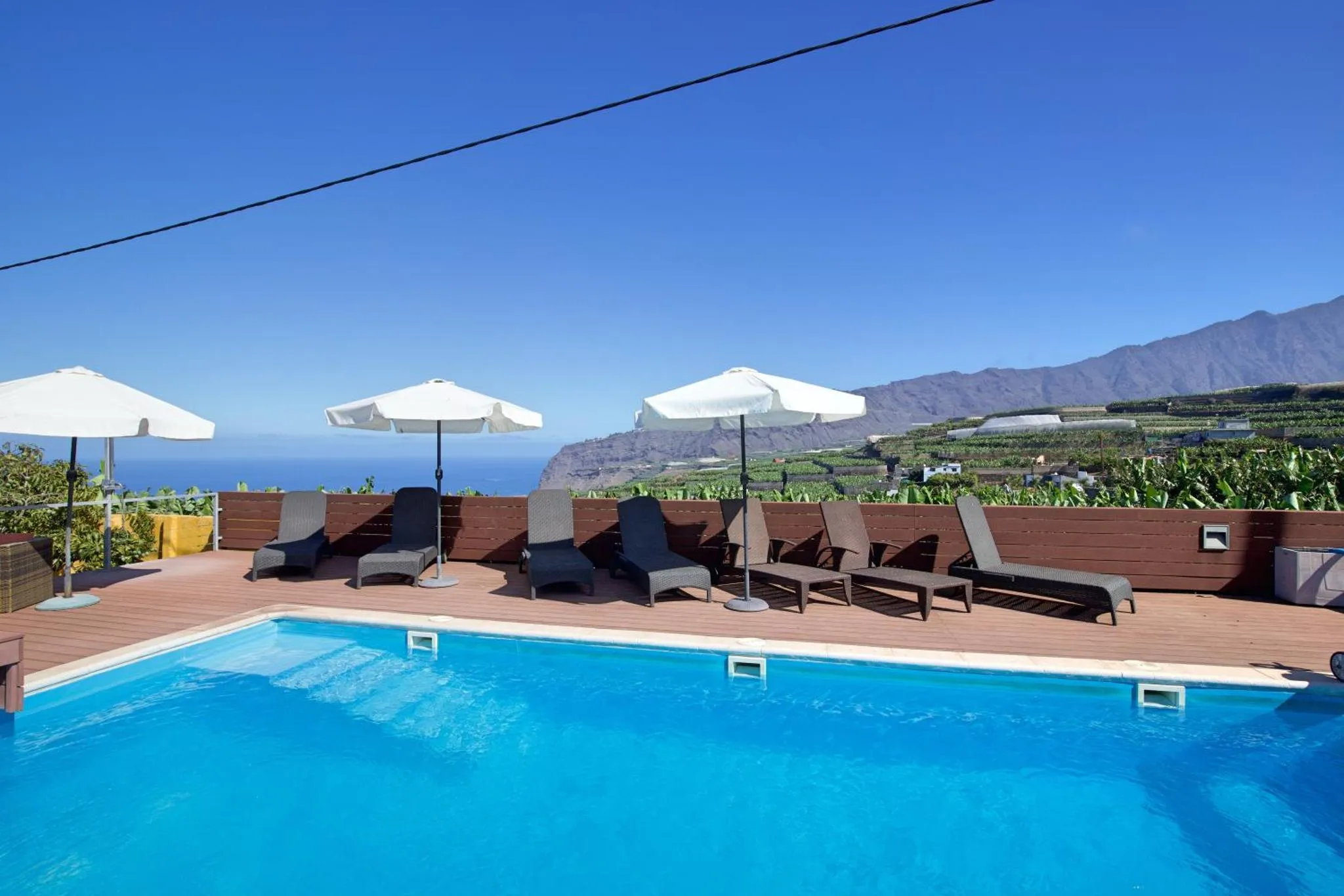 Transats et parasols bordent une piscine turquoise avec vue sur la mer et les montagnes.
