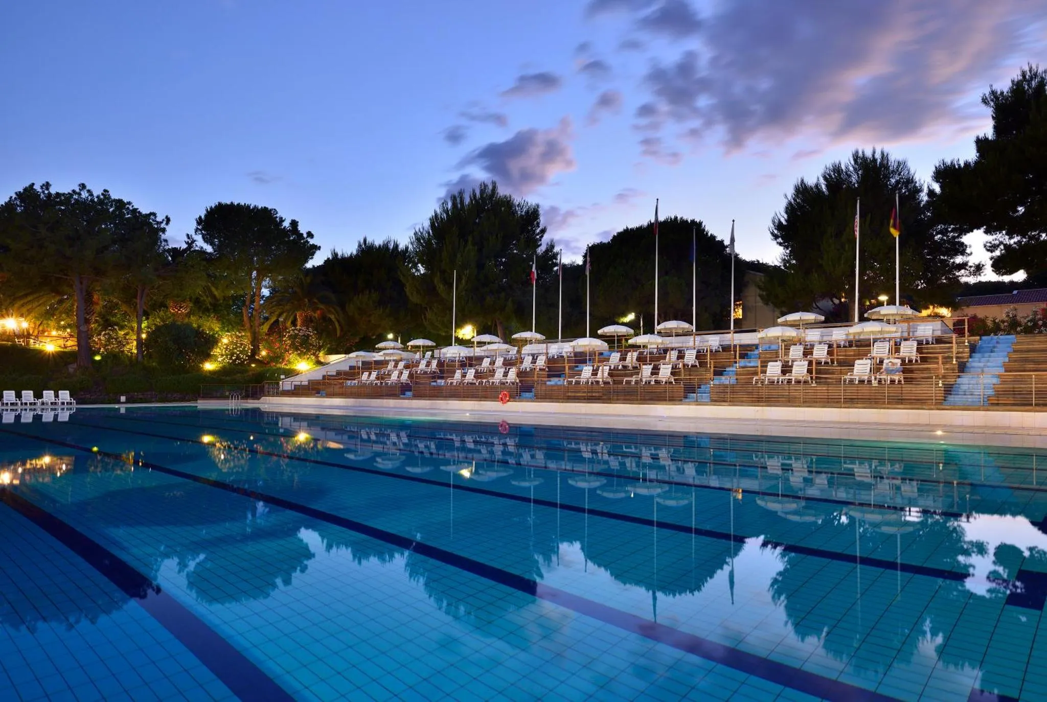 Une piscine extérieure avec des transats alignés au bord, au crépuscule.