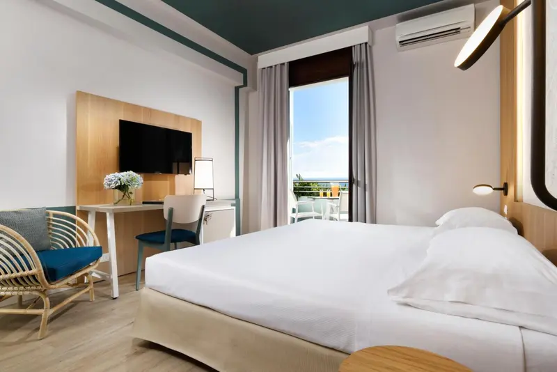 Une chambre lumineuse avec un lit blanc et un bureau près d'une fenêtre.