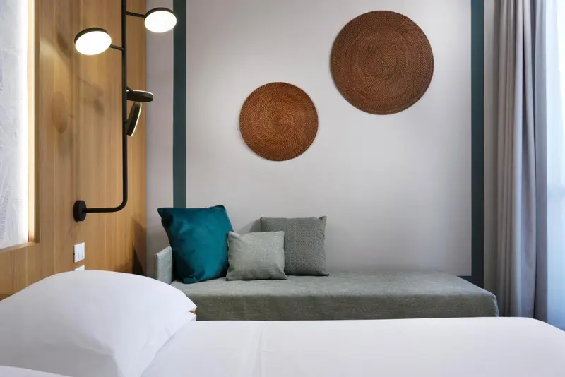 Un lit blanc avec des oreillers et un canapé gris ornent une chambre décorée de manière moderne.