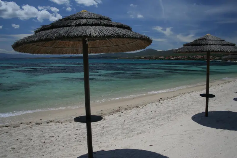 Parasols sur une plage de sable blanc bordée d'une eau turquoise.