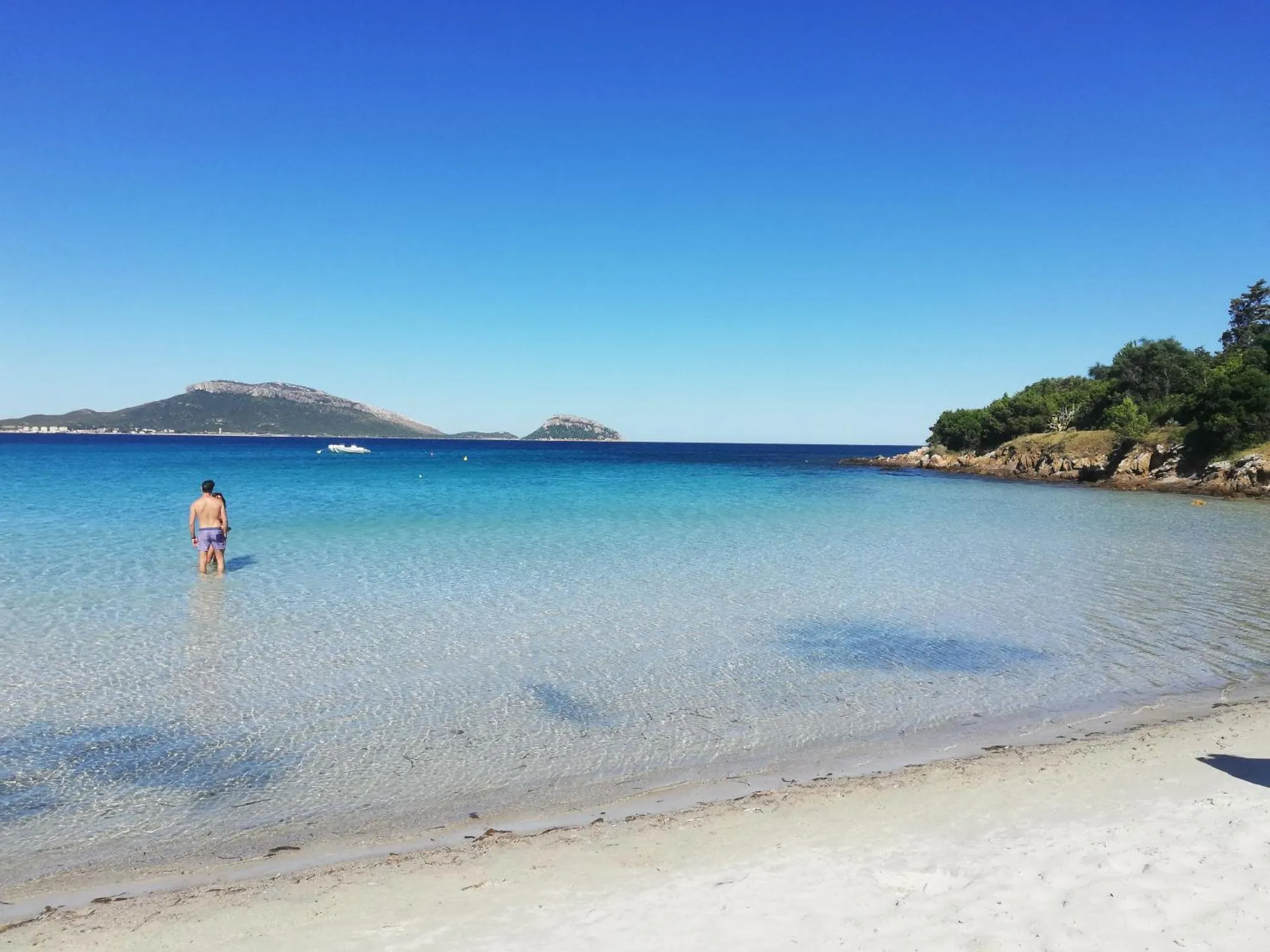 Une personne se tient dans une eau turquoise peu profonde sur une plage de sable clair.