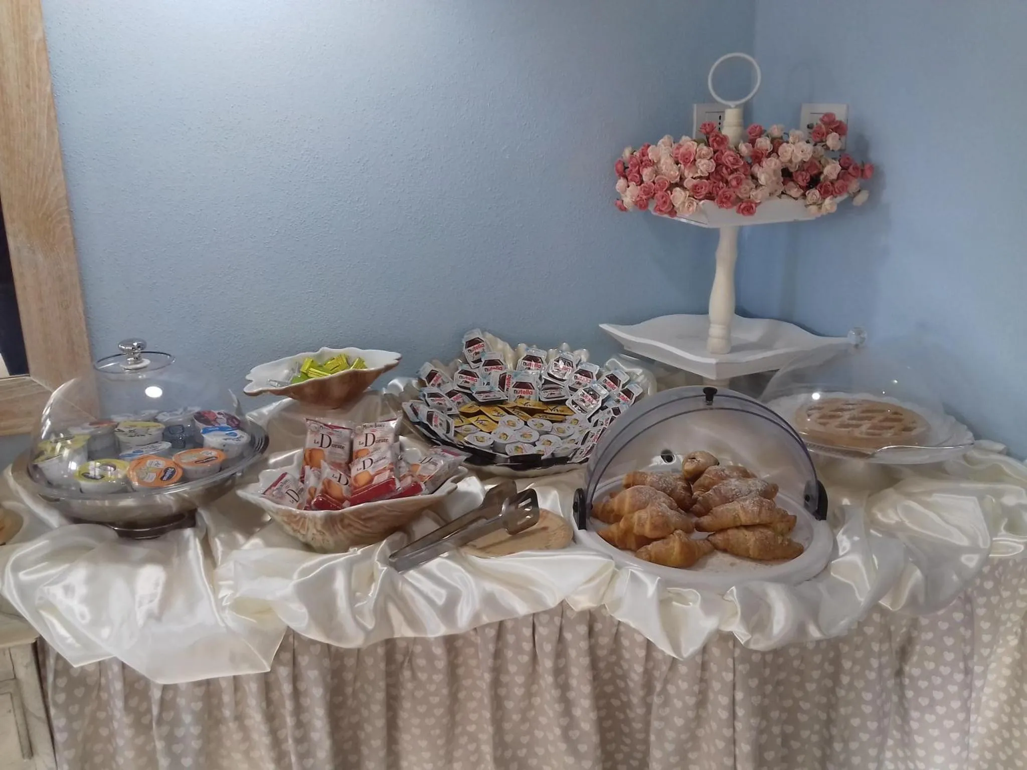 Une table garnie de viennoiseries et de confitures est présentée sur une nappe décorée.