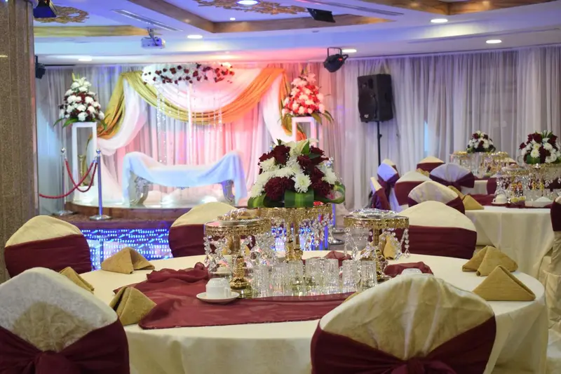 Une salle de réception décorée pour un événement avec des tables dressées et des arrangements floraux.