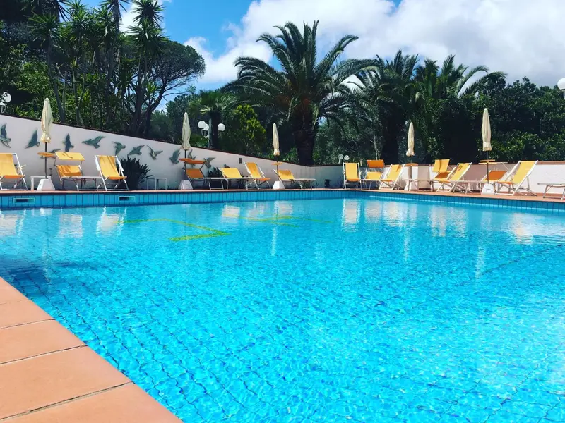 Transats alignés au bord d'une piscine turquoise sous un ciel bleu nuageux.