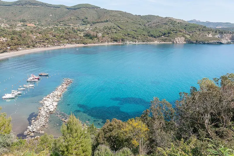 Vue aérienne d'une crique turquoise bordée de bateaux et de végétation.
