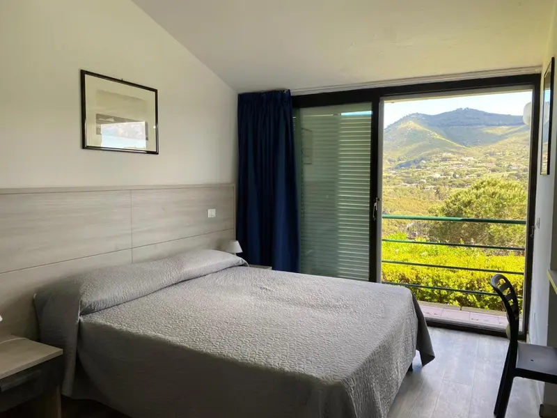Une chambre lumineuse avec un lit simple donnant sur un paysage montagneux.