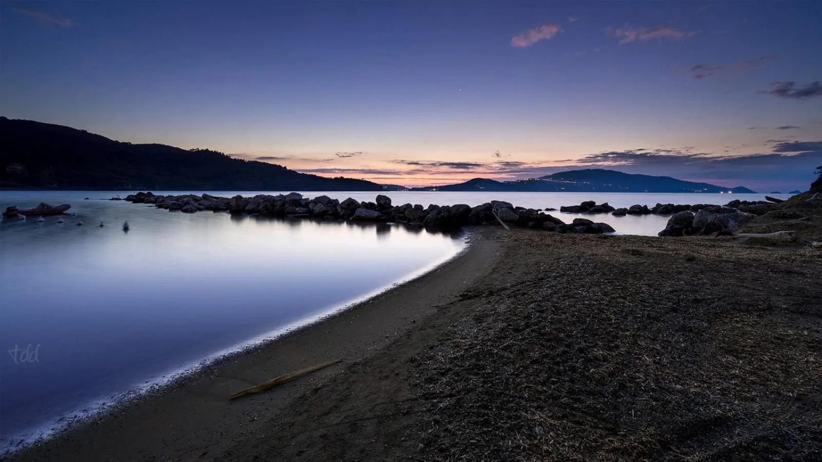 Plage de galets au crépuscule avec vue sur la mer et les montagnes.